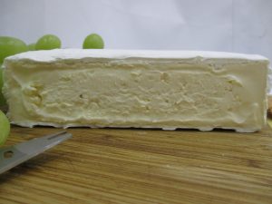 A cross section of brie cheese on a cheese board with grapes in the background. Brie is an example of soft-ripened cheese