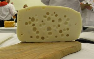 A cross section of cheese with eyes. Eyes are characterized bylarge holes scattered throughout the cheese