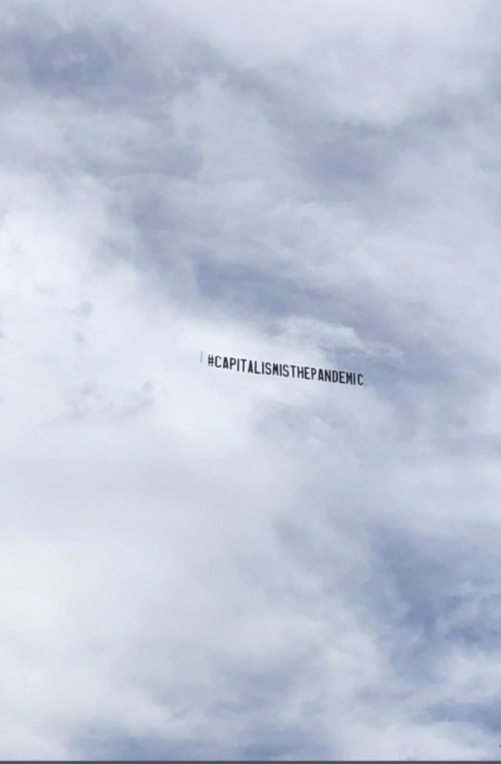 image: Floating among a cloudy sky, the words #Capitalismisthepandemic float, as if pulled by a force.