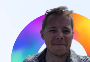 A photo of Dr. Daniel Gillis in front of a rainbow arc.